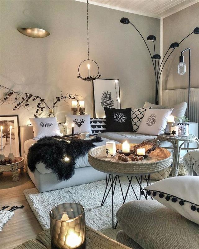 originalus apvalaus stalo austas viršus baltas kokoninis kilimas pilka sofa su dekoratyvinėmis pagalvėlėmis šviesiai pilkos sienos juoda lempa jaukus žiemos deko