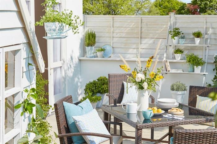 Dekoratyvinis sodo stalas ir kėdės su mėlynomis pagalvėlėmis, vazos ir gėlių vazonai, lauko terasų idėjos, nedidelis modernus sodo išdėstymas