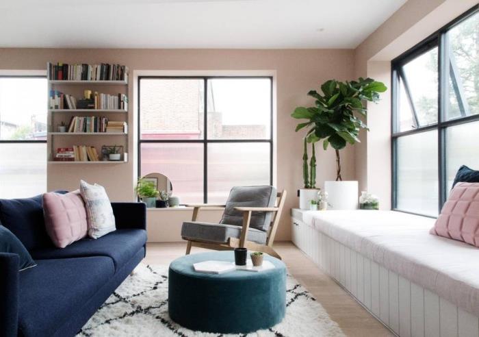 svetainė su rožinėmis sienomis su baltomis lubomis ir šviesaus medžio parketu, tamsiai mėlyna sofa ir turkio spalvos išmatos