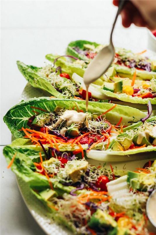 Ideja za hiter recept za večerni aperitiv, vegetarijanski recept za mavrične tacose v listih solate s svežo zelenjavo, okrašeno s humusom in rdečo omako
