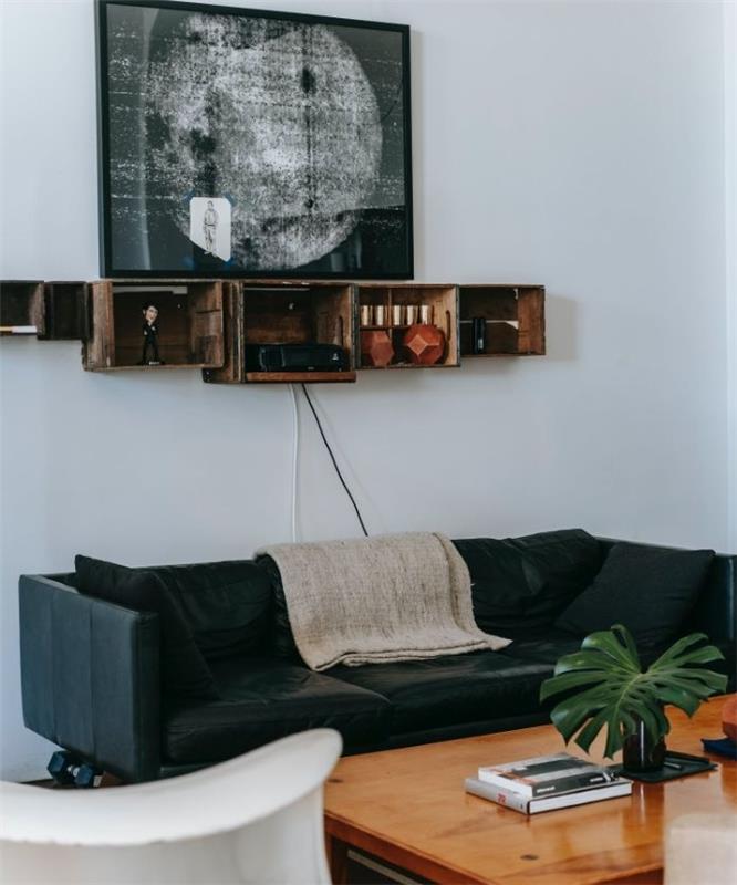 regeneruotos pramoninės sieninės lentynos pramoninio stiliaus svetainėje su juoda odine sofa ir mediniu kavos staliuku