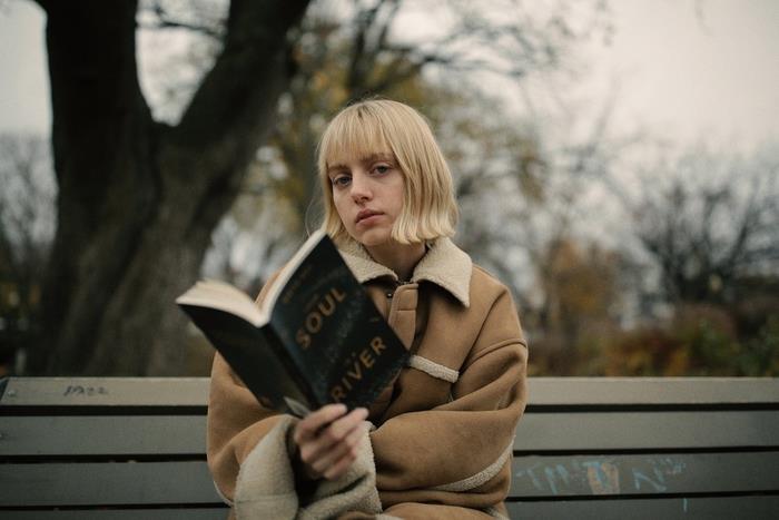 Idea per dei tagli capelli medi di colore biondo con frangia, ragazza con libro in mano seduta su una panchina