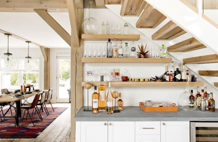 odprte lesene police pod lesenimi stopnicami, bela kuhinjska omara in siva delovna plošča, ki se odpira v jedilnico