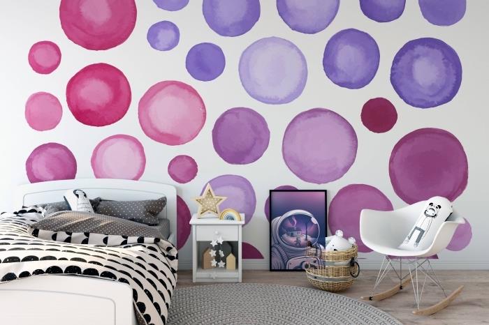 dekoravimo idėja vaiko kambarys su apvaliu pilku kilimu ir balta lova, balta tapetų sienų danga su purpuriniais ir rožiniais apskritimais