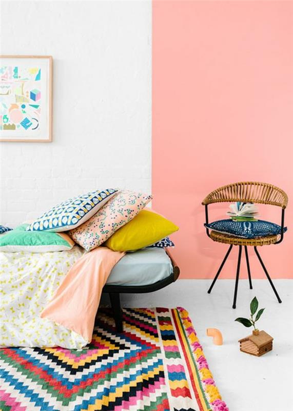 kelių spalvų etninis kilimas, pastelinė rožinė siena, dekoratyvinės pagalvės, kaimiška kėdė