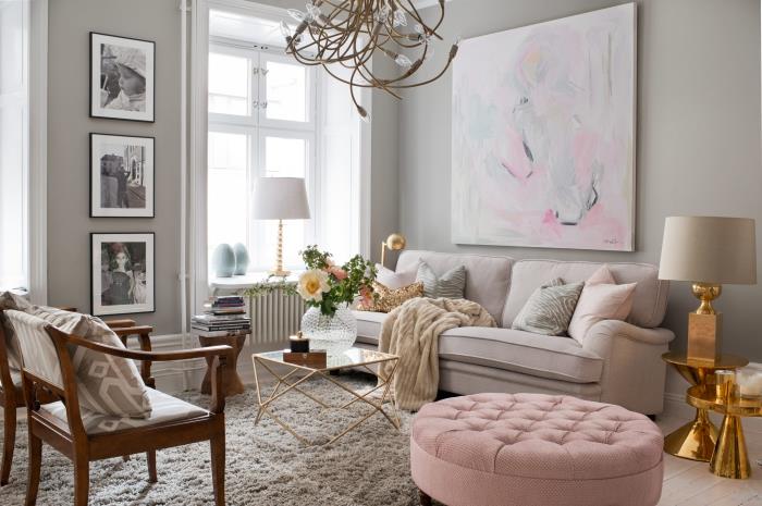 pilkas svetainės dekoras su šviesiai rožine sofa ir tamsiai rudos spalvos mediniu foteliu, apvalių stalų modeliu ir vario dizaino lempa