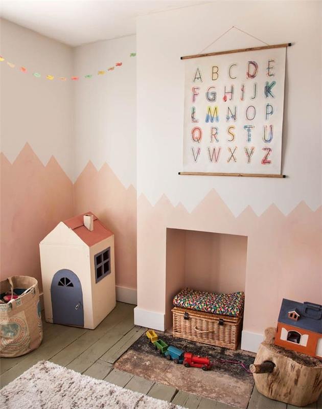 senovinis miegamasis su montessori atmosfera, siena perdažyta šviesiai ir tamsiai rožine spalva, dėvėtas parketas, originali žaislų dėžutė, kartoninis namas, medžio kamienas kaip taburetė, krepšys ant grindų