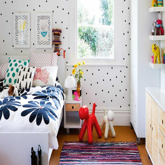 duvar dekorasyonu küçük siyah noktalı beyaz duvar kağıdı, mavi ve pembe etno tarzında halı, çiçek desenli beyaz ve mavi battaniyeli yatak, PVC'de ahşap efektli beyaz mobilyalar