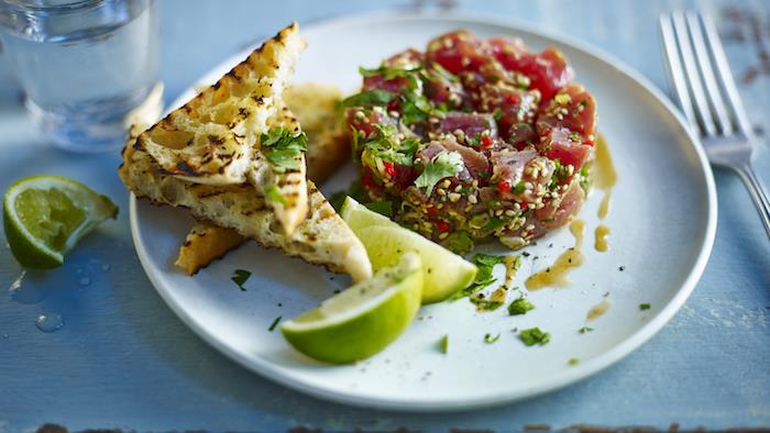 tatarski tatarski tuna in sezam s svežimi zelišči, postreženimi z opečenim kruhom in rezinami limone, hladna predjed