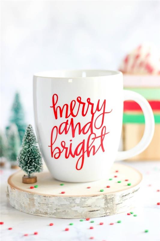 Noel ağacı heykelcik yanında ahşap kütük üzerinde kırmızı harflerle özel beyaz kupa Mutlu Noeller metni, Noel için hediye fikri