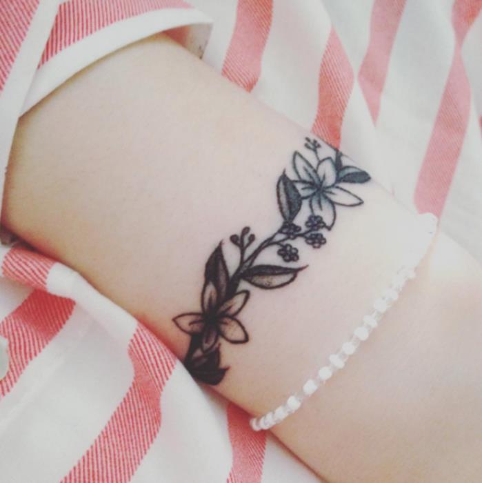 riešo apyrankės tatuiruotė, elegantiška grafinė moters tatuiruotės idėja, gėlių šaka, juodas rašalas
