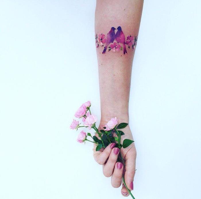 moters tatuiruotė, žydinti šaka, rožių gėlės ir paukščiai rožinės ir violetinės spalvos, elegantiška apyrankės tatuiruotės idėja