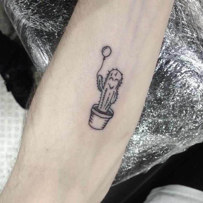 diskretiška tatuiruotė, mažas juodas kaktusas puode su maloniu veidu ir laikantis balioną