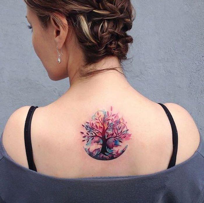 ženska tetovaža na hrbtu, drevesni simbol integritete, siva bluza, pričeska z lepljenimi pletenicami