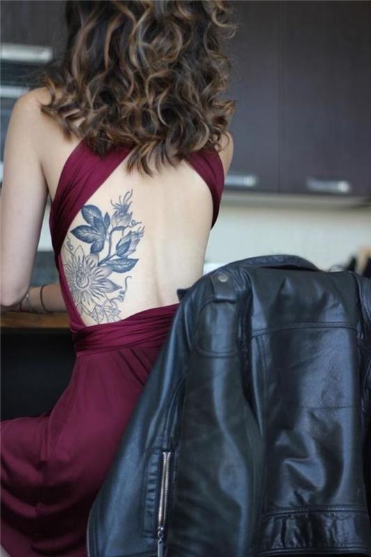 Ženska tetovaža na hrbtu s cvetličnimi motivi, bordo obleka, kodrasti lasje, tetovaža s črnimi rebri