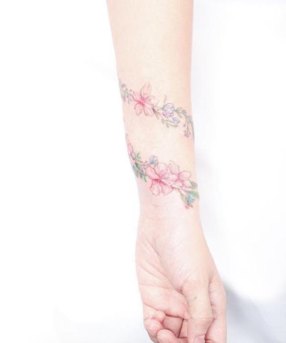 moters apyrankės tatuiruotė, žydinti šaka, apvyniota aplink riešą, rožių gėlės, estetiškas spalvingas dizainas