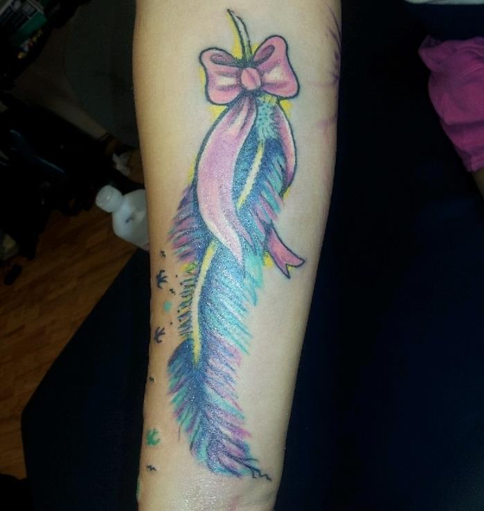 Ideja o ženski tetovaži, risanje na koži, ženska tetovaža z rožnatim trakom in večbarvnim peresom