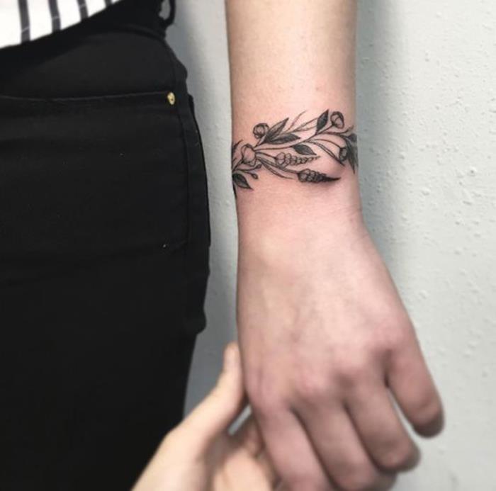 Moteriška apyrankės tatuiruotė ant riešo, žydinti šaka, piešimas juodu rašalu, moteriška tatuiruotė