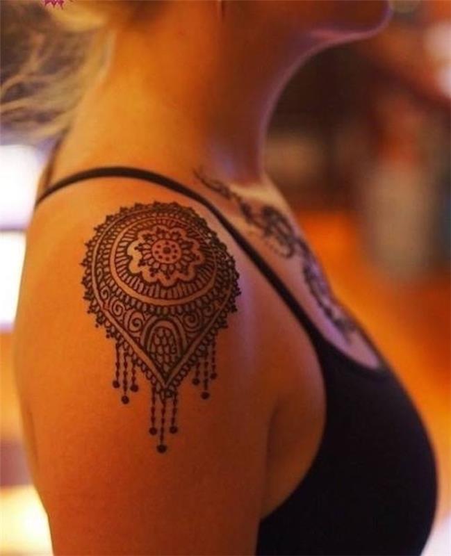 ženska tetovaža na rami, mandala z obeski, črna brezrokavnica, črna tetovaža z izrezom