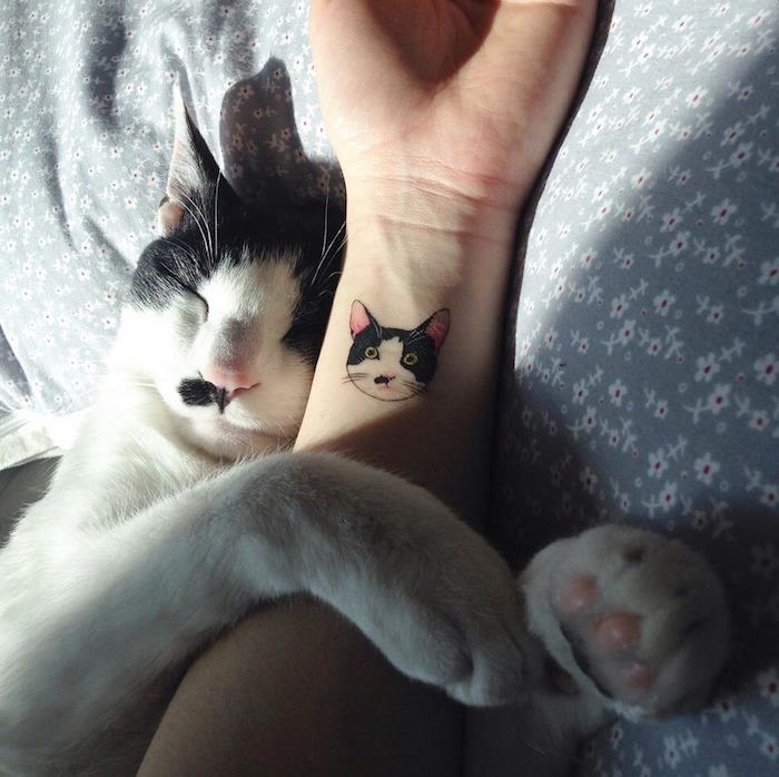 majhna tetovaža, spi mačka na postelji v odeji s sivim cvetličnim vzorcem, barvna risba na koži
