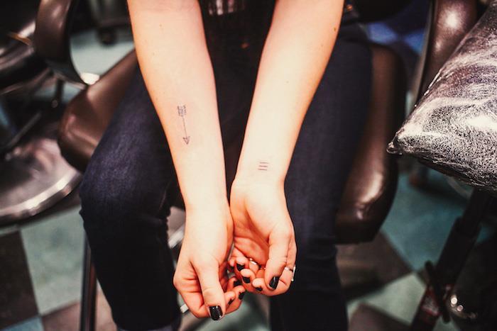 ženska tetovaža z roko, črni usnjeni stol, črne ženske hlače, črna manikura, majhna tetovaža na zapestju