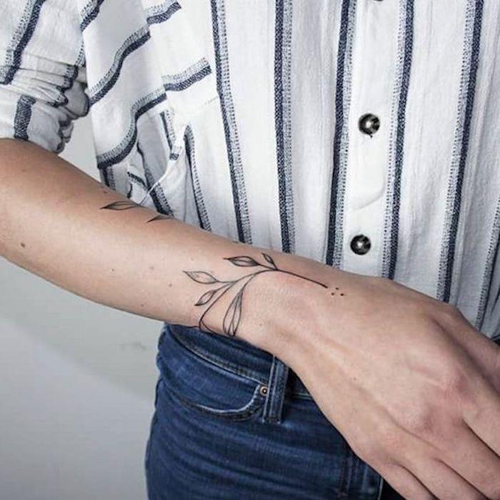 črtasta srajca, modre kavbojke, diskretna tetovaža rastlinskega motiva, ženska tetovaža z roko