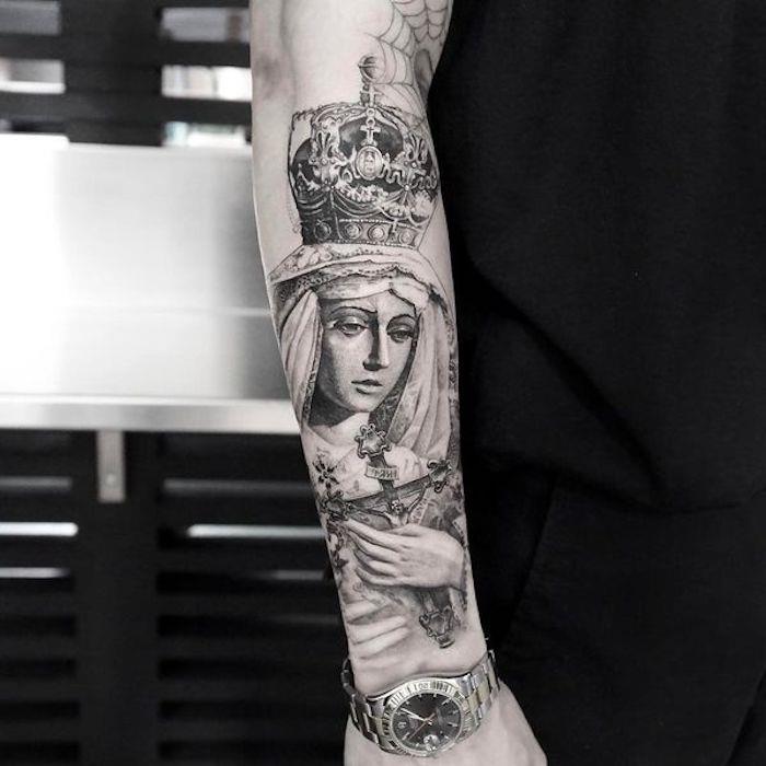 Il braccio di un uomo con une grande tattoo religioso con donna e croce in mano