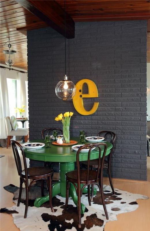 Piccola sala da pranzo con un tavolo verde rotondo e sedie, decorazione da parete con una lettera gialla
