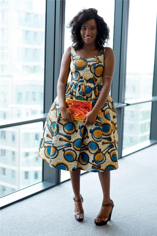 vsestranski voščeni model za casual ali profesionalen videz, sežgana obleka z ženskim krojem in afriškimi vzorci v modri in oker barvi, usklajena s kovinsko torbico