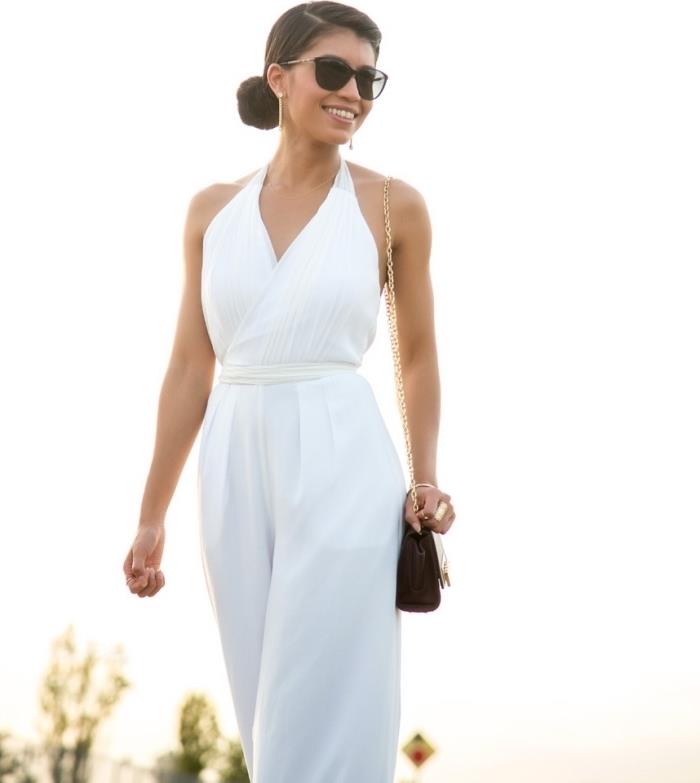 stilinga moteris su baltu kombinezonu su diržu kartu su rankinė ir juodais akiniais