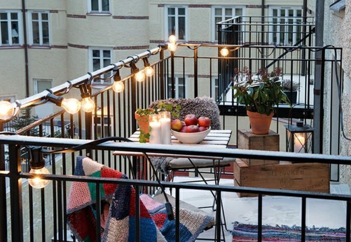 siyah korkuluklu veranda, bir dizi parlak ampulle kaplı, eşleşen sandalyeli küçük kare ahşap masa, ön sundurma dekorasyon fikirleri, dekoratif ahşap kasalar ve saksı bitkisi