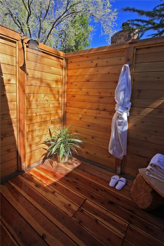 majhna kopalnica na dvorišču z rjavimi lesenimi tlemi in stenami, fiksna zunanja kovinska prha