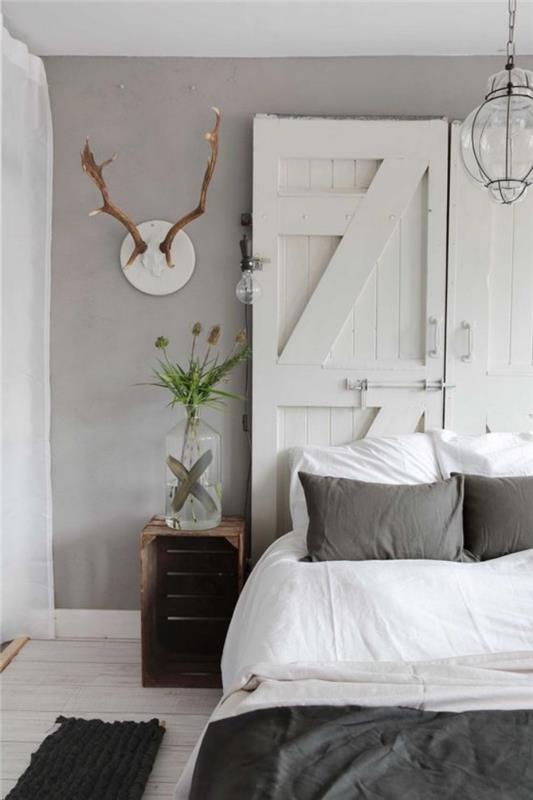 naredite vzglavje v belih vratih, sivo -belo posteljnino, beljen parket, sivo barvo sten, dekoracijo sten jelenovega roga, nočno omarico v lesenem zaboju