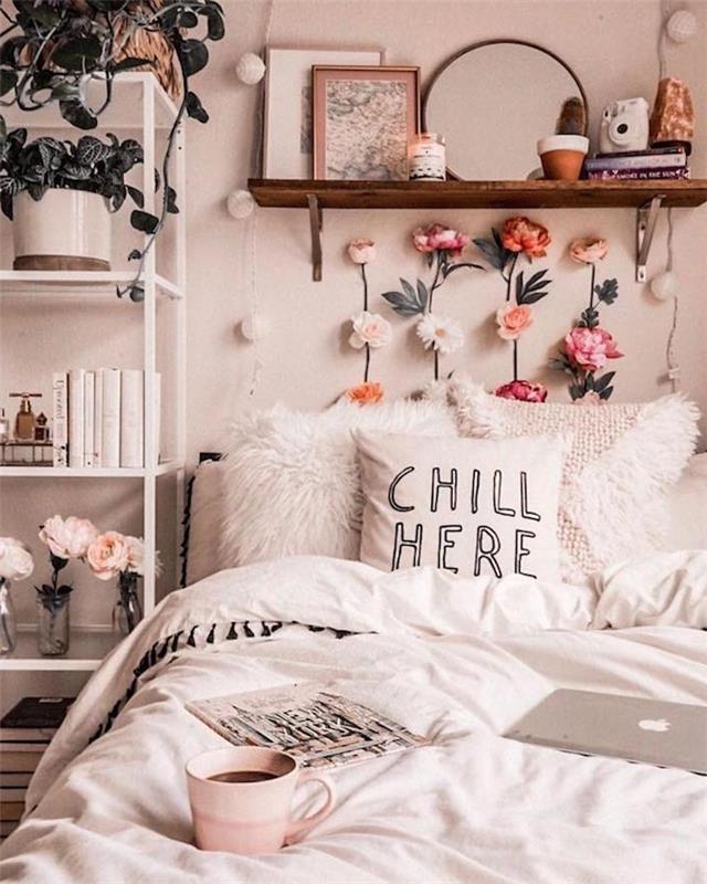 medinės jaukios lovos lentynos galas, padengtas baltu lovos komplektu, gėlių galvūgalis, lova prie baltos knygų ir augalų lentynos