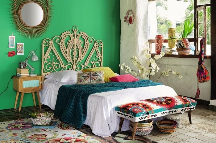 natūralus miegamojo dekoras su žaliomis sienomis su smėlio spalvos plytelėmis išklotomis grindimis ir augalinio pluošto baldais, įvairiaspalvis suoliukas su medinėmis kojelėmis