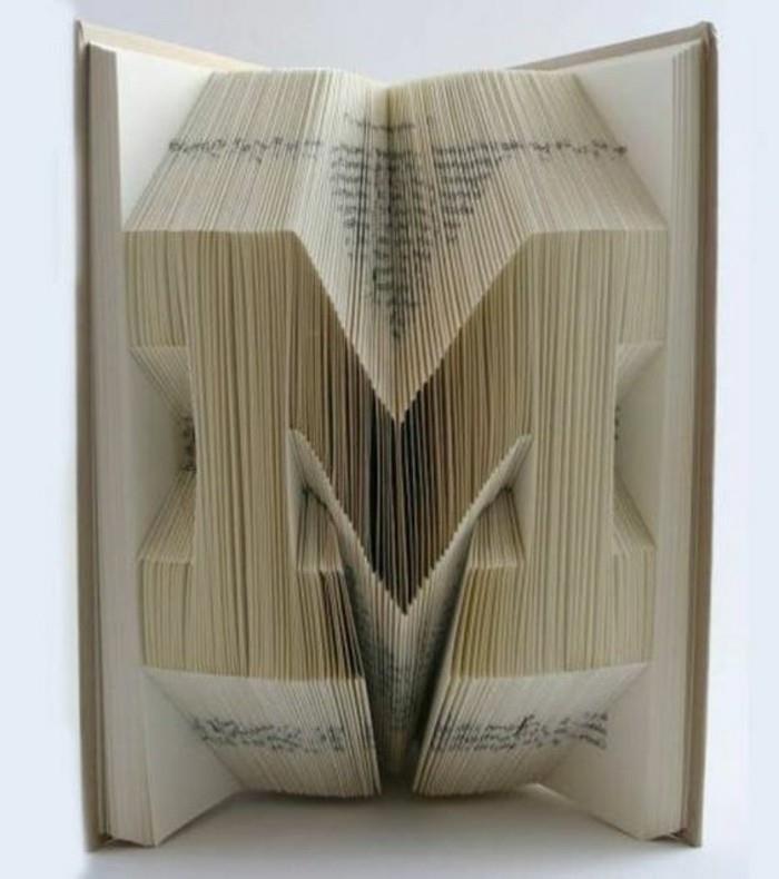 črka m, narejena iz prepognjenih strani, v odprti knjigi s trdimi sivobelimi platnicami