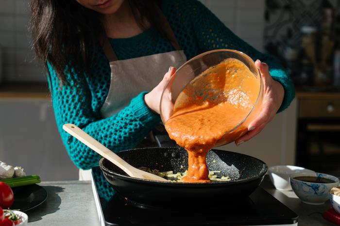 trinti pomidorai stikliniame dubenyje, pomidorų sriubos receptas, užpilti salierais ir svogūnais juodojo padažo keptuvėje, medinė mentelė šone