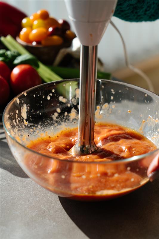 pomidorai stikliniame dubenyje, sutrinti rankiniu mikseriu, pomidorų sriuba, pilkas stalviršis, neryškus fonas