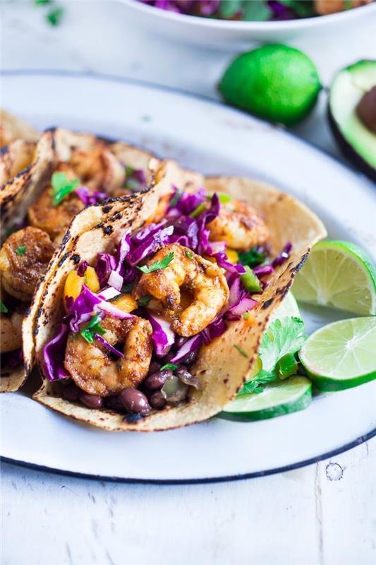 tortilijos įvyniojimai, užpildyti kopūstais, keptomis krevetėmis, ant baltos lėkštės, taco ingredientai, laimo skiltelės šone