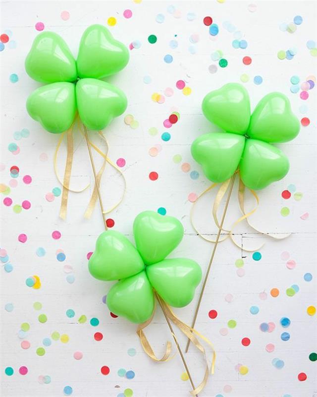trys žalios spalvos dobilai širdies formos balionuose, spalvingi konfeti, auksinė juostelė