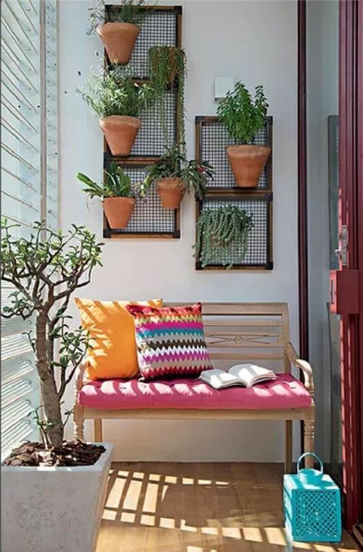 ön sundurma dekoru, pembe kapaklı ahşap bank, çok renkli iki minder ve bir kitap, ön veranda dekoru, duvarda birçok saksı bitkisi