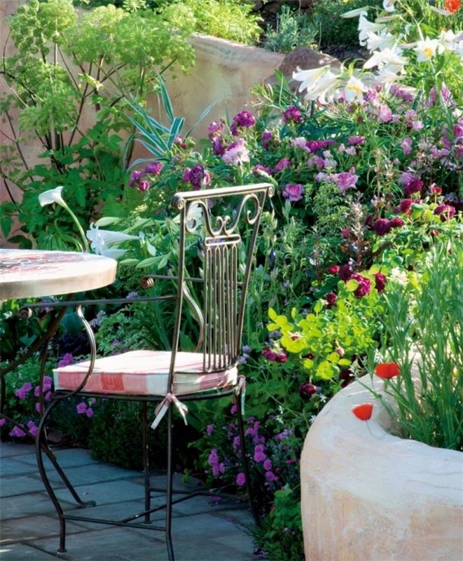 klestinti augmenija, sutvarkyta anglų stiliumi, keli žydintys krūmai, gėlės, sodo baldai, sudaryti iš metalinio stalo ir kėdės