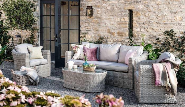 rotango baldų komplektas priešais didelį akmeninį namą su pagalvėlėmis ir rožinėmis gėlėmis