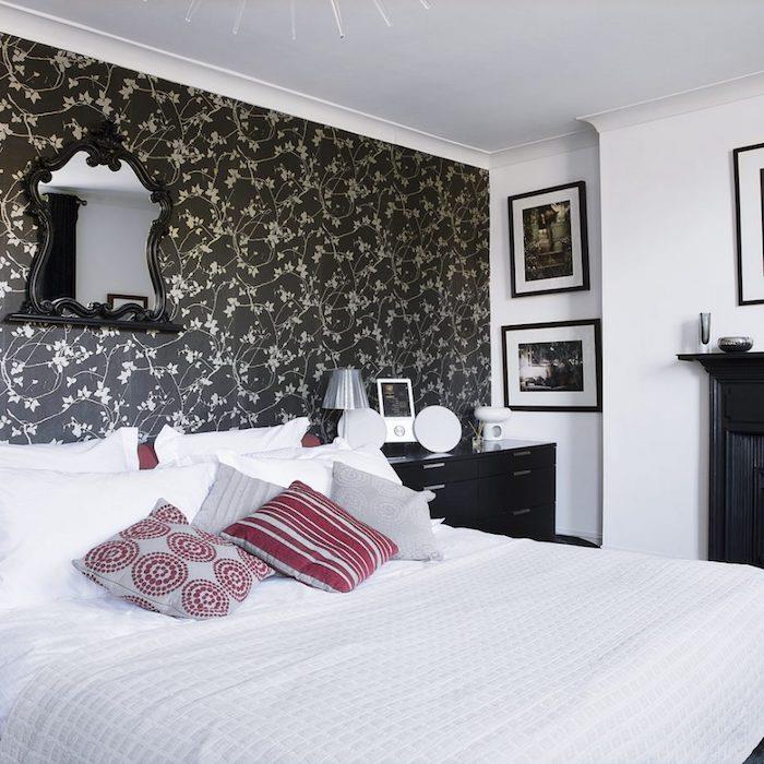 tek duvarda yatak odası halısı fikri, siyah arka planda çiçek deseni, beyaz yatak takımı, gri ve kırmızı minderler, siyah şifonyer, vintage ayna