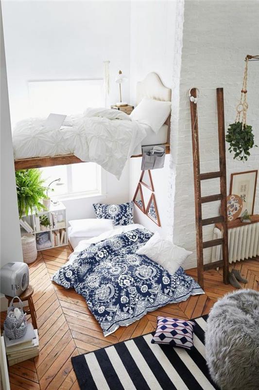 9m2 miegamasis, boho prašmatnaus stiliaus studento miegamojo dekoras, lovos užtiesalas su mėlynai baltais moliniais raštais, rudos medinės kopėčios, vertikalus baltas ir tamsiai mėlynas dryžuotas kilimas