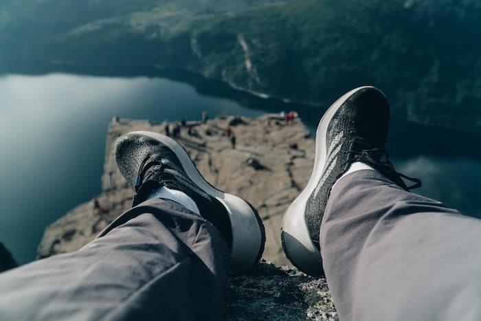 žmogus, sėdintis ant uolos, ilsisi ir vilki juodus sportbačius