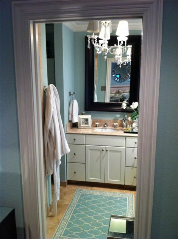 gražiai mėlynas vonios kambario kilimas su baroko liustra ir balto medžio komoda