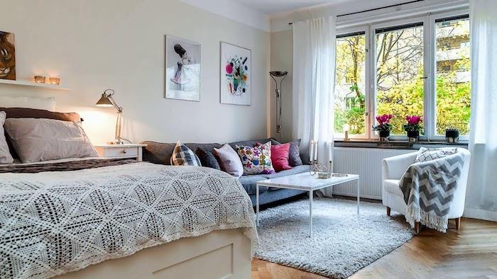 majhna dnevna soba in spalnica, eleganten dekor s sivo -belo posteljo, siv kavč, bela mizica, beli naslanjač