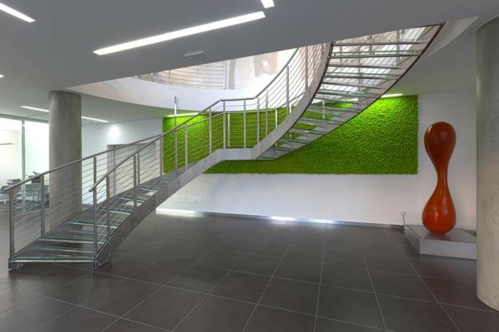 interjero žalia siena, visuomeninis pastatas su pusiau pasukamais laiptais iš lengvo aliuminio metalo, grindys padengtos taupe spalvos plytelėmis, abstraktus meninis darbas, raudona figūra