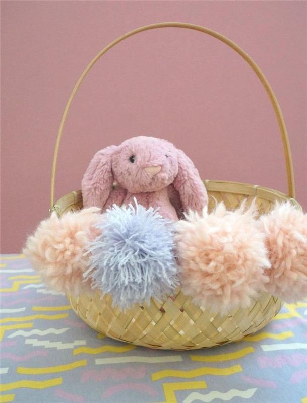 ponponlarla süslenmiş hasır bir sepet ve sevimli bir peluş tavşan paskalya dekorasyonu
